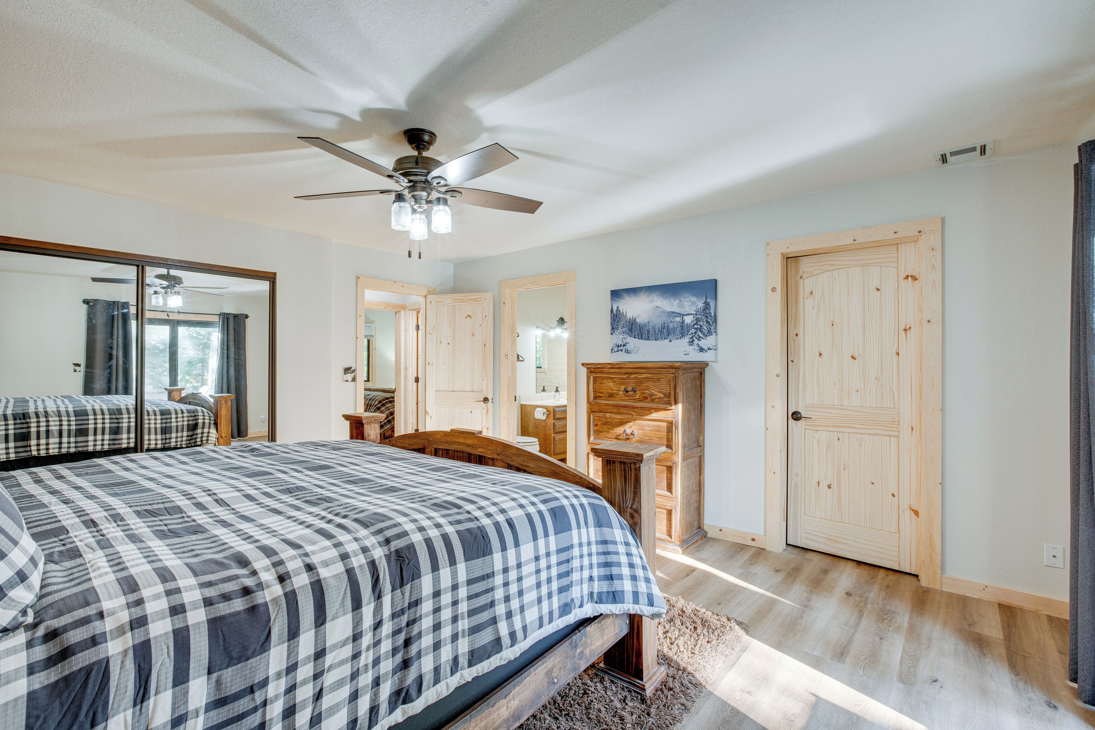 Een slaapkamer met een groot bed, een plafondventilator, een houten dressoir en een deur met een schilderij erboven.