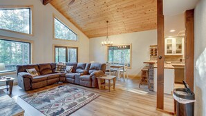 Ein geräumiges Wohnzimmer mit einer großen Eckcouch, Holzböden und großen Fenstern mit Blick auf den Wald.