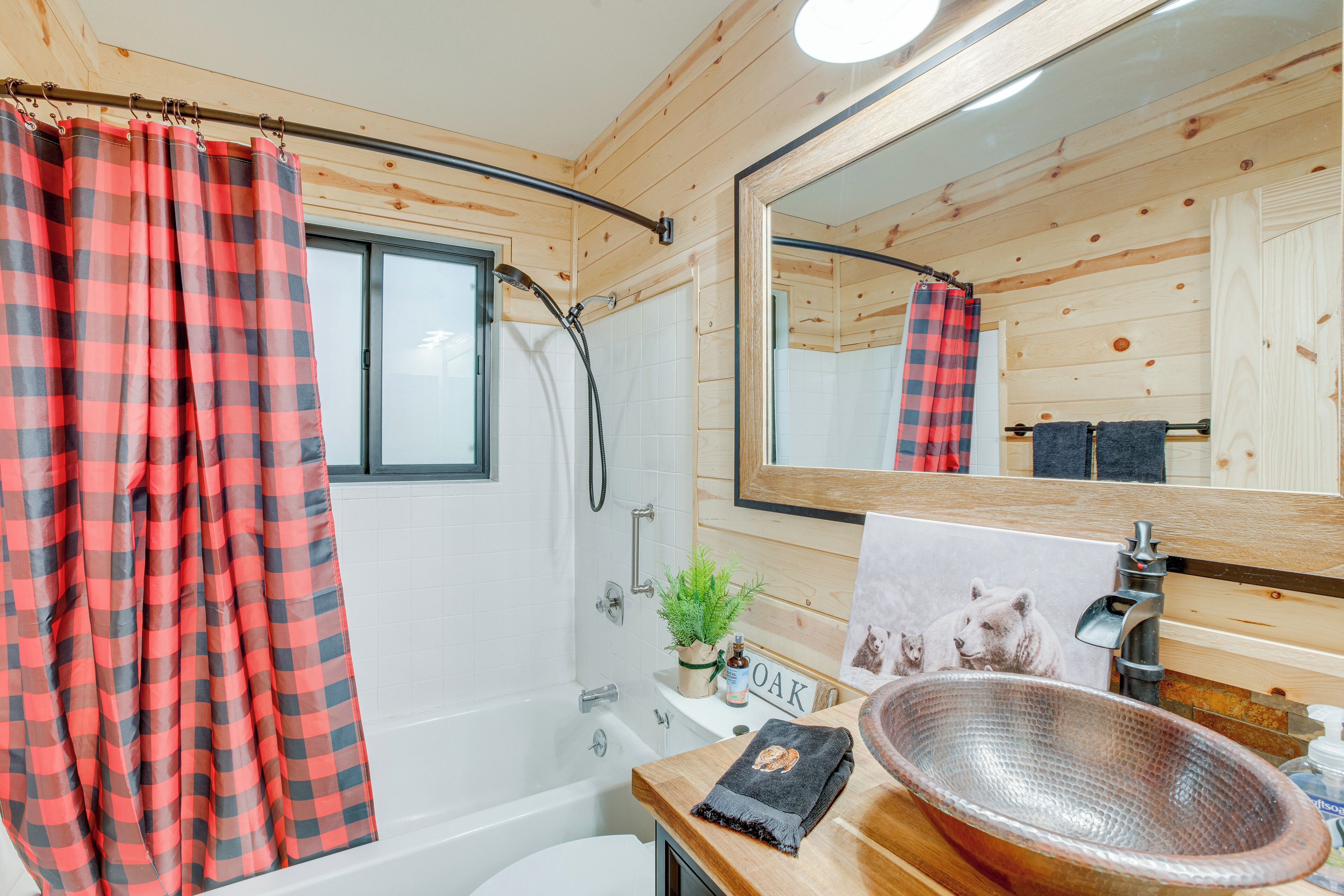 A bathroom with a wooden interior, a bathtub, a shower, a sink with a copper basin, and a mirror.