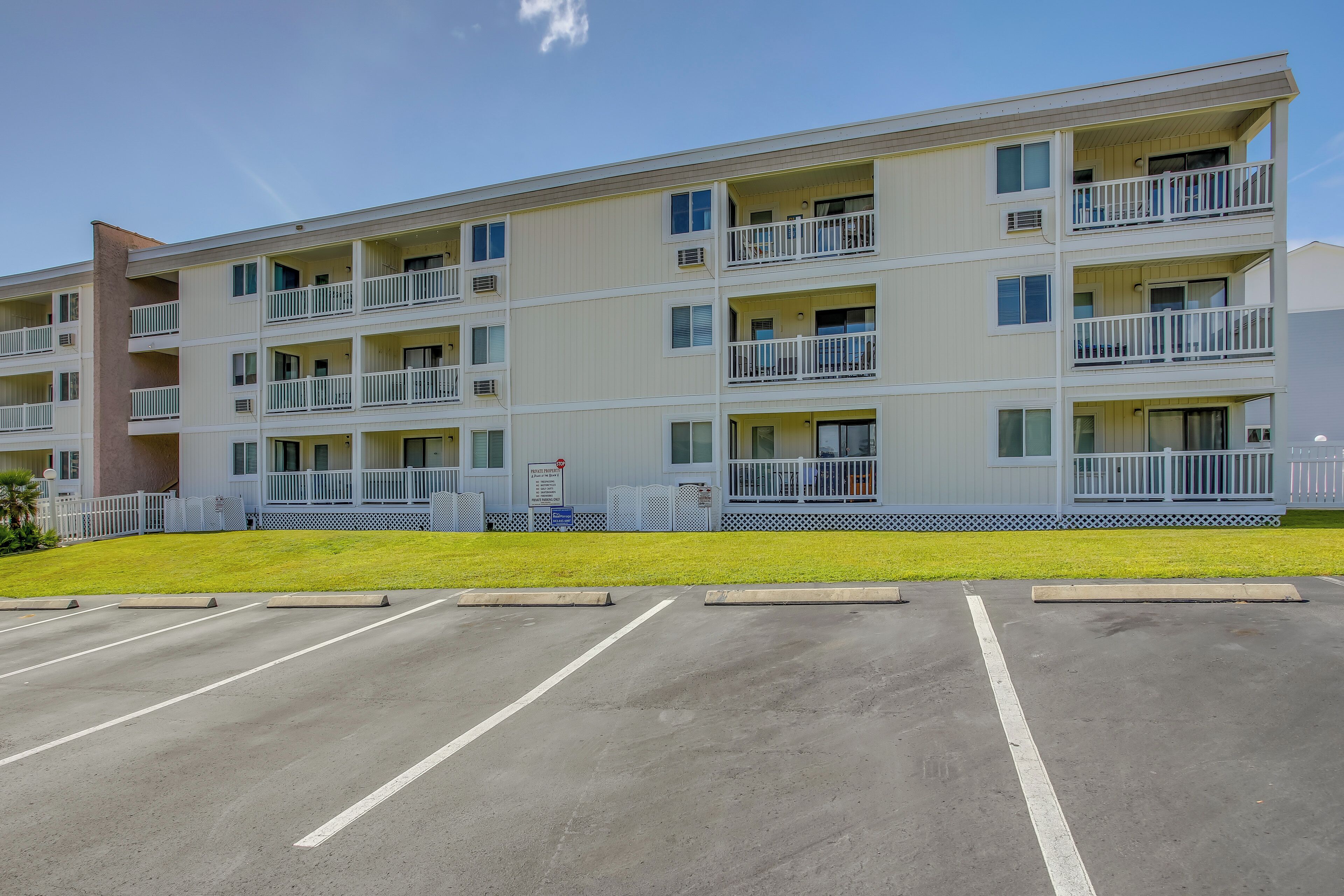 A multi-story hotel with balconies, a parking lot, and a grassy area.