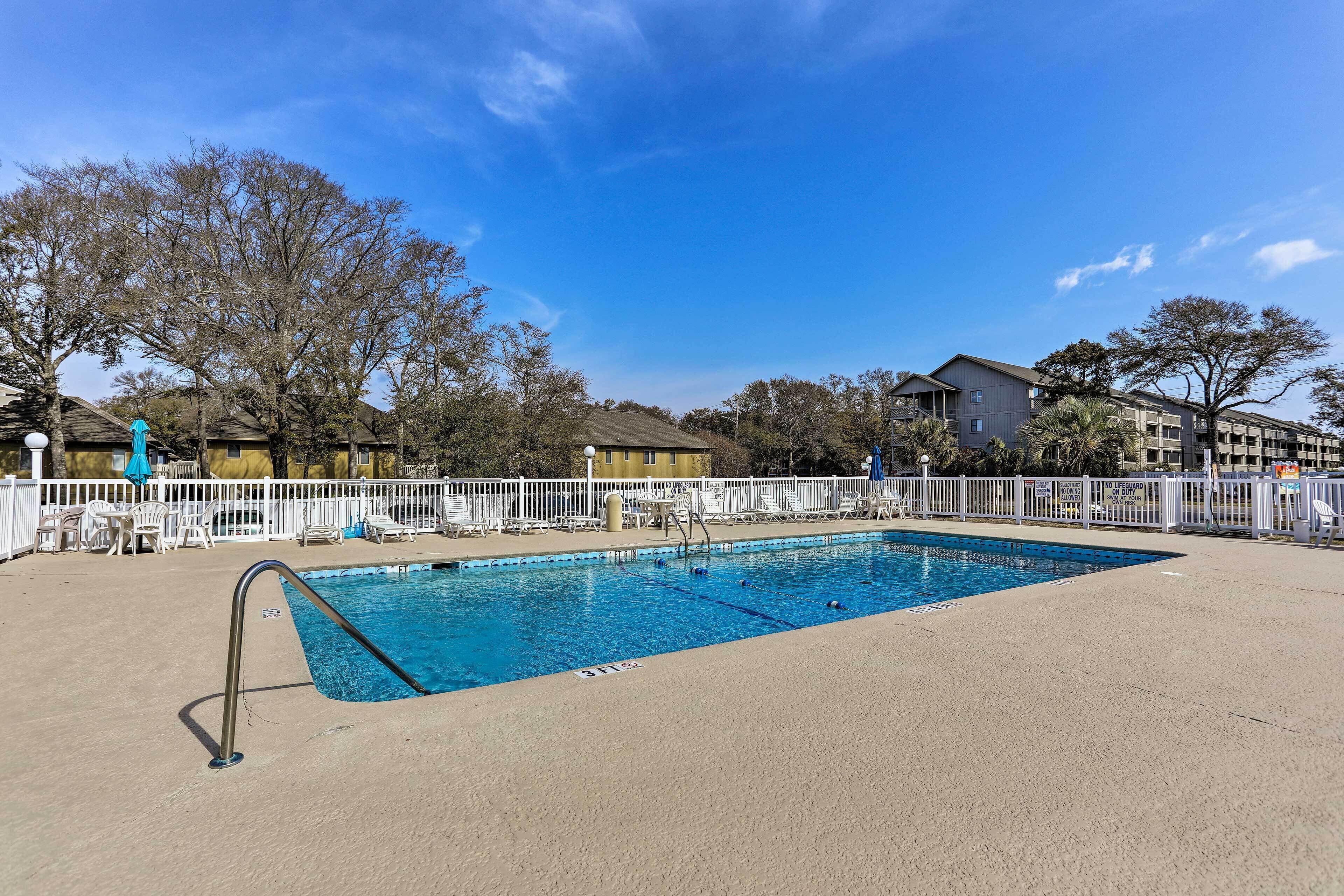 A rectangular swimming pool with a metal ladder on one side, surrounded by a white fence.