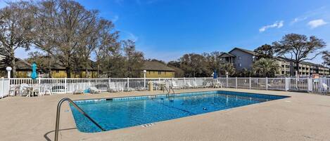 A rectangular swimming pool with a metal ladder on one side, surrounded by a white fence.