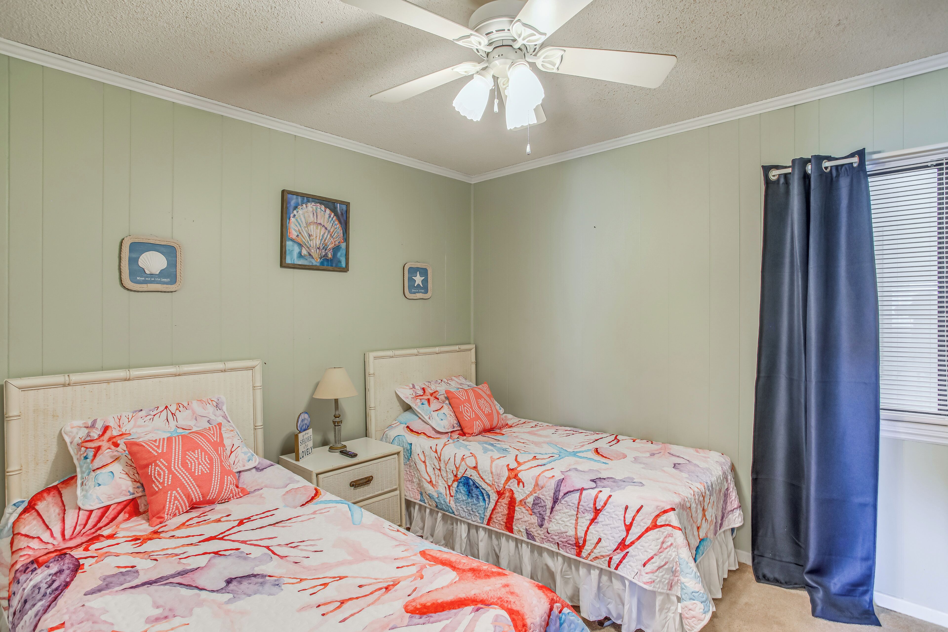 A bedroom with two beds, a ceiling fan, and a window with curtains.