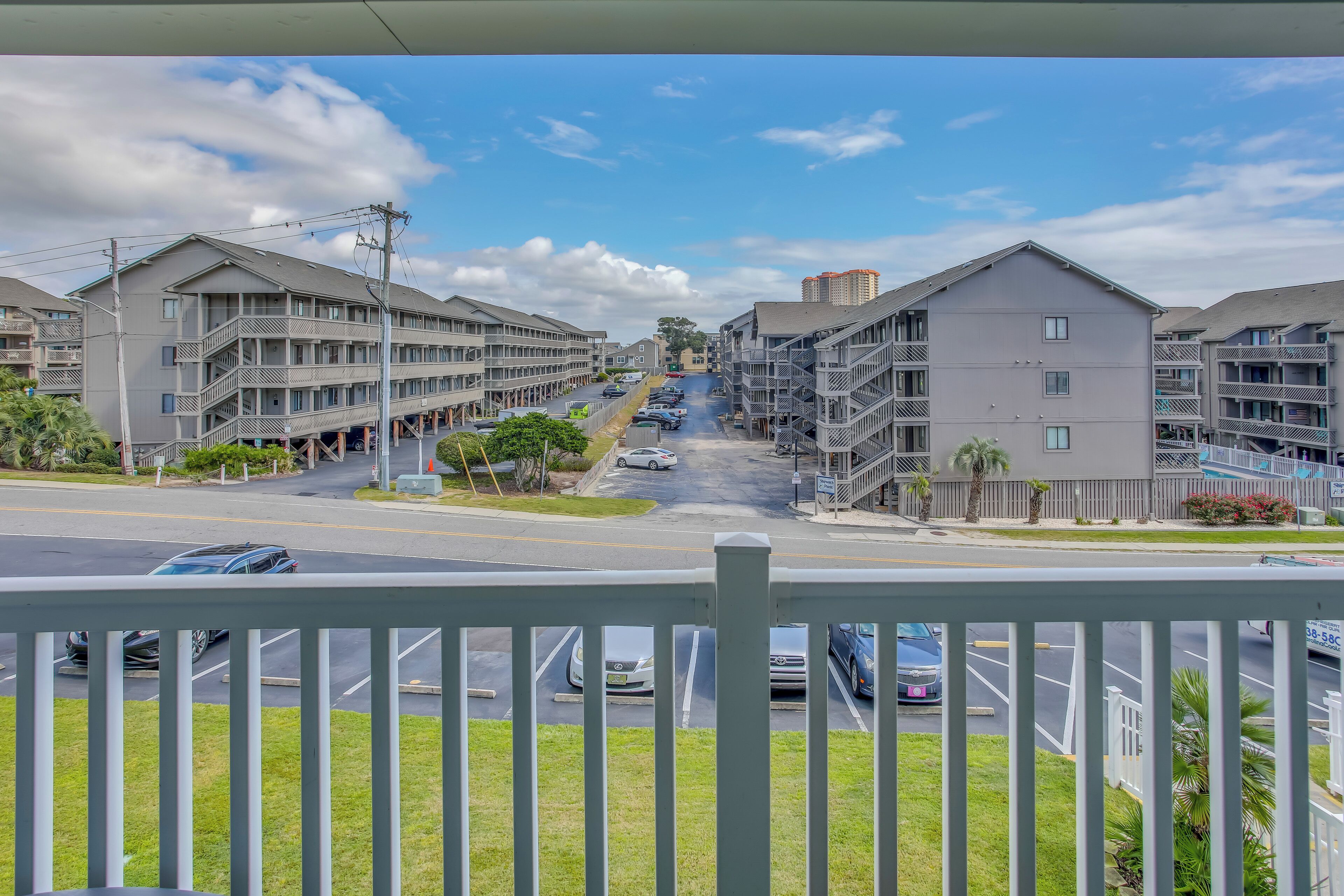 A multi-story residential building with balconies, a parking lot, and a clear sky.