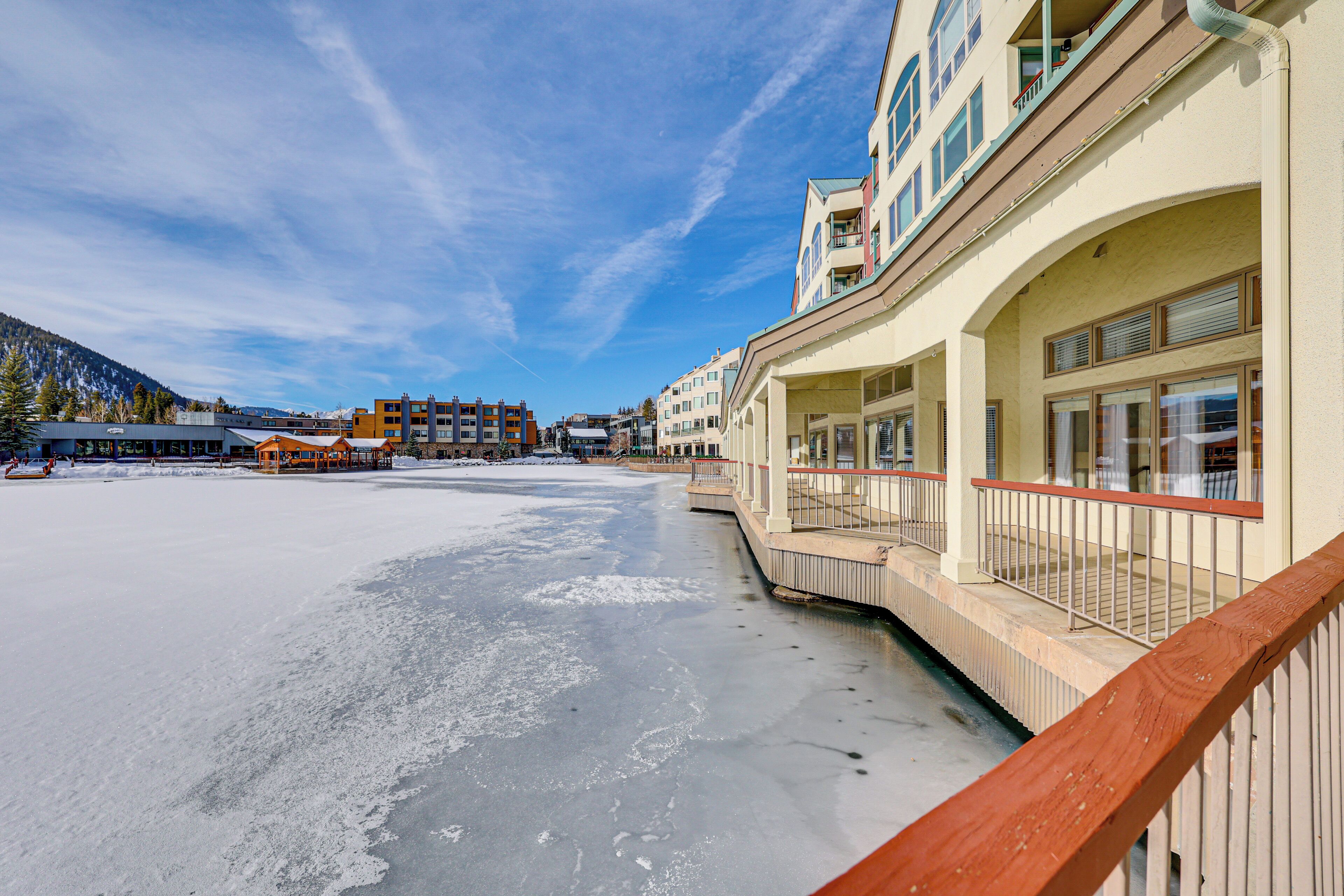 Hotel aan het water met balkon met uitzicht op een bevroren wateroppervlak, aangrenzende gebouwen en een heldere lucht.