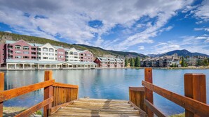 Une jetée en bois mène à un hôtel situé au bord de l’eau, composé de plusieurs bâtiments. On y trouve un lac paisible et, en arrière-plan, des montagnes.
