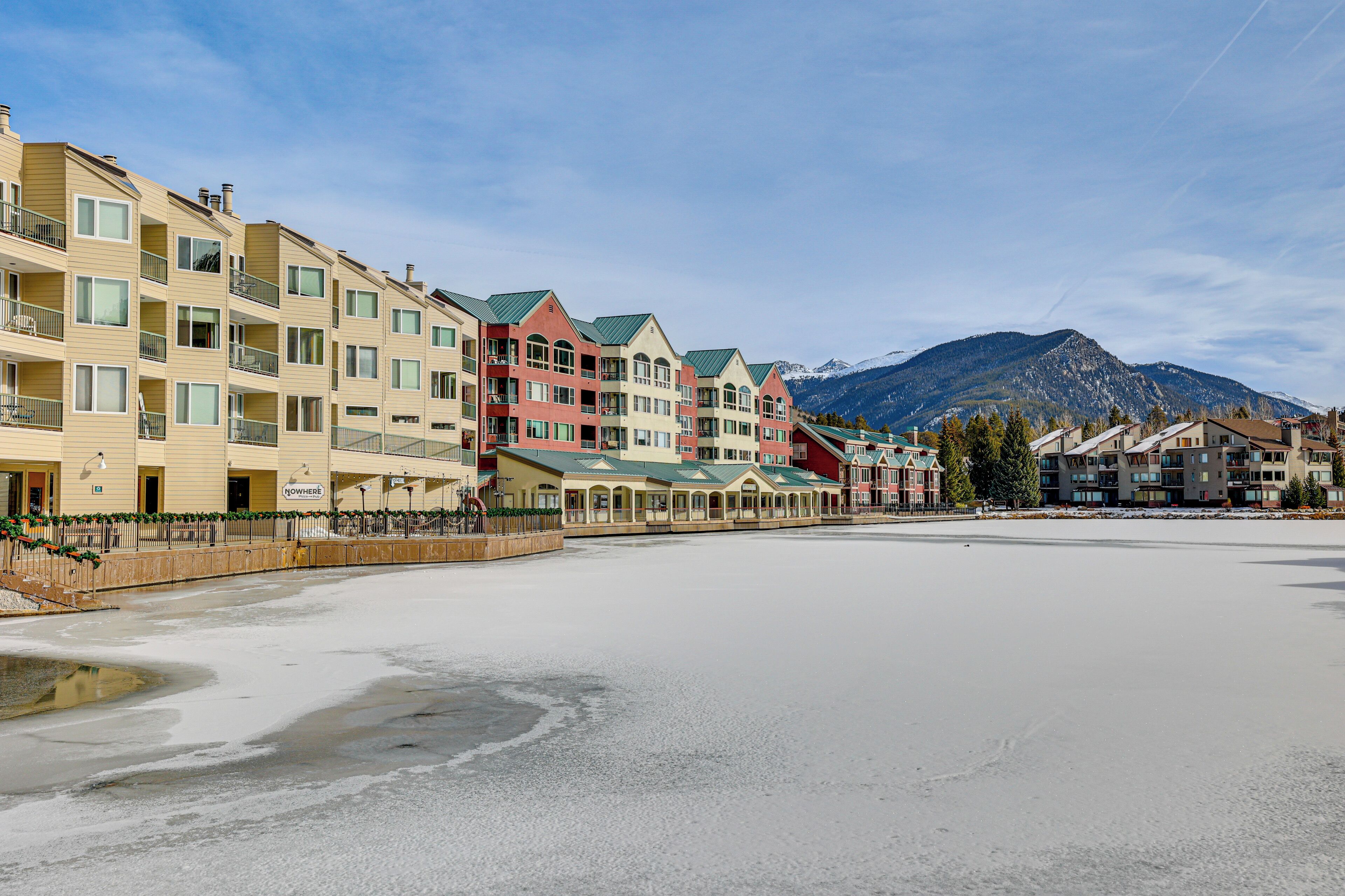 A row of multi-story buildings with balconies, a flat paved area in the foreground, and mountains in the background.