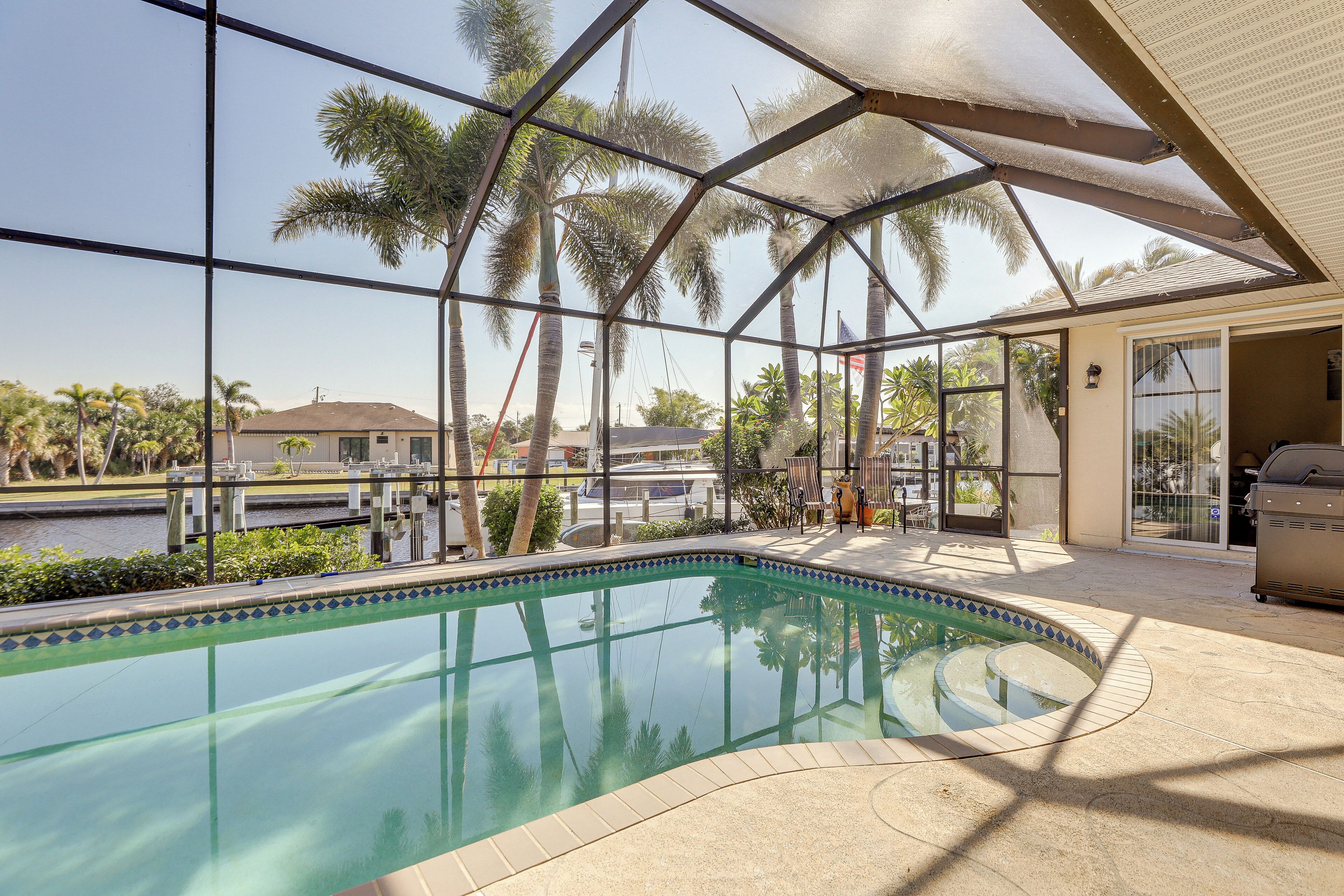 Piscina com cobertura de vidro, palmeiras e vista para um corpo d'água.