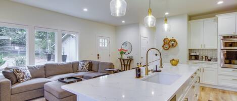 A modern kitchen with white cabinets, a large island with a sink, and pendant lighting.