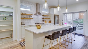 A modern kitchen with white cabinetry, a central island with bar stools, pendant lighting, and a view of the outdoors. - Private Yard & Fire Pit! Modern Kirkland Abode (Kirkland)