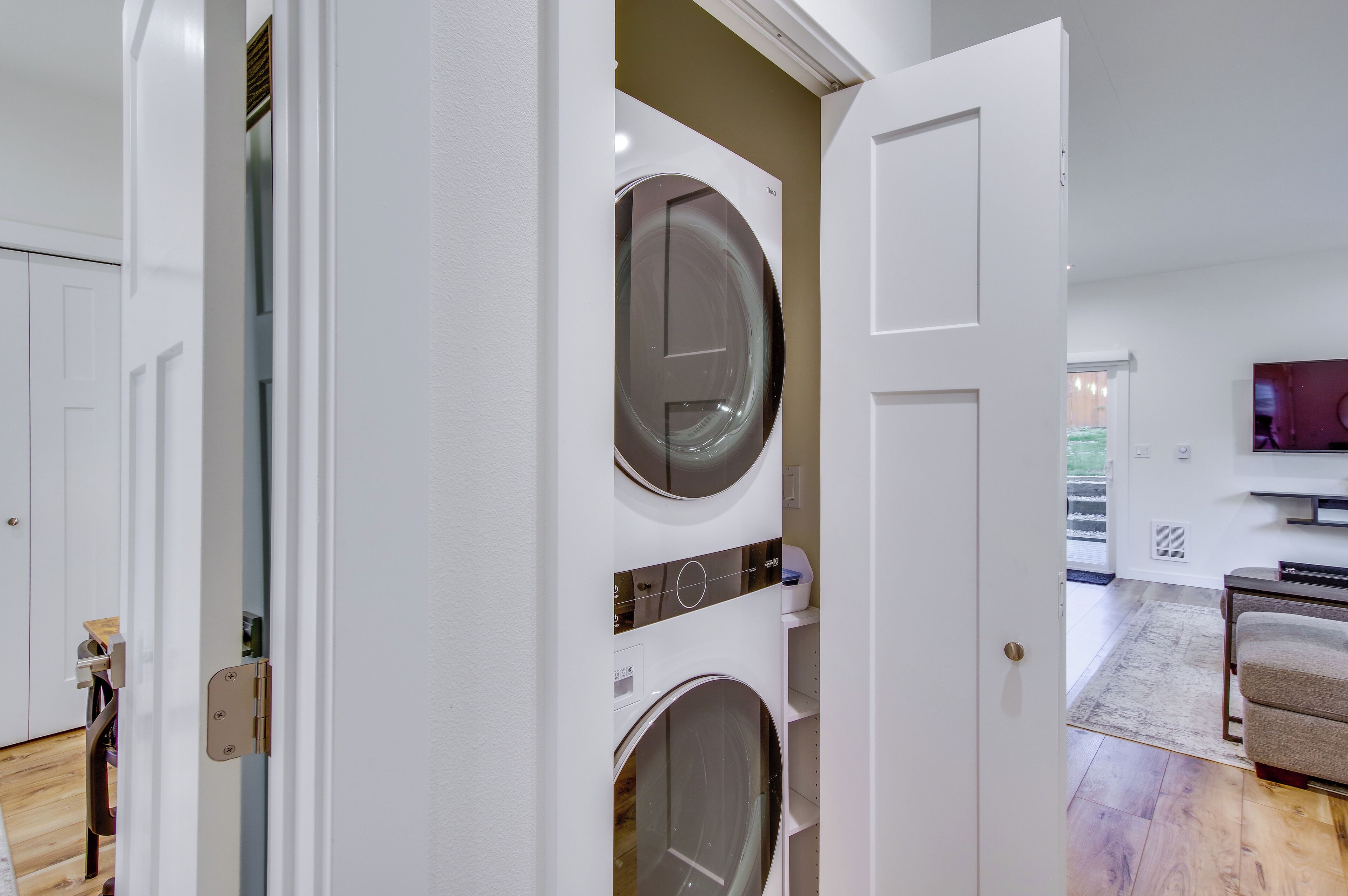A laundry room with stacked washers and dryers, a door leading to a living area with a couch and a TV.