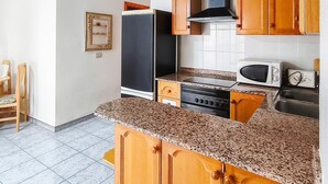 Une cuisine avec des meubles de rangement en bois, un four à micro-ondes, une cuisinière et un évier.