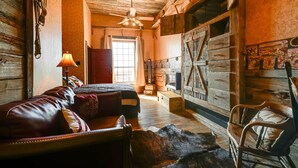 Una stanza rustica con soffitto in legno, un letto con testiera rossa, una sedia di legno, una stuoia di pelliccia e un caminetto.