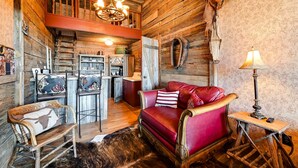 Un interno rustico con una scala in legno, un divano in pelle rossa, una poltrona a dondolo in legno e un angolo cottura.