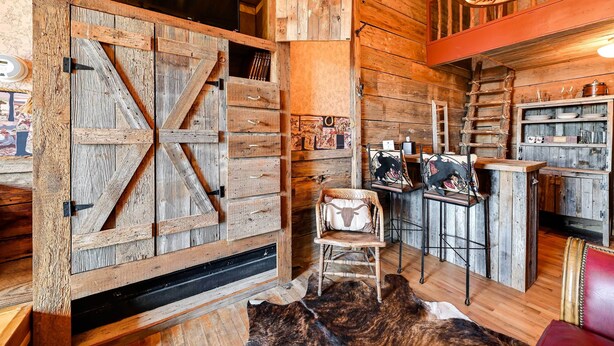 Un interno rustico in legno con un'ampia porta a casone, un'area bar in legno e un divano in pelle.