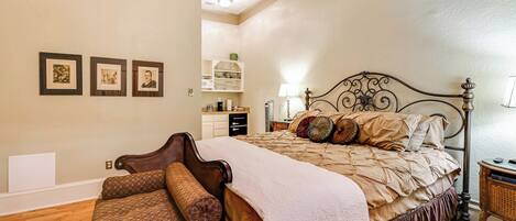 A bedroom with a bed, a chair, a nightstand, and a wall with three framed pictures.