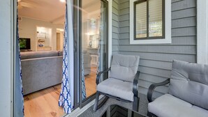 A covered patio area with a sliding glass door leading to a living room, a gray sofa, and two gray cushioned chairs. - Walkable Calabash Condo w/ Pool Access! (Calabash)