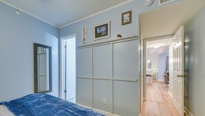 A bedroom with a bed, a wardrobe, and a hallway leading to a kitchen. - Walkable Calabash Condo w/ Pool Access! (Calabash)