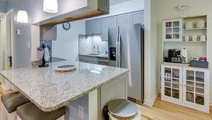 A modern kitchen with granite countertops, stainless steel appliances, and a breakfast bar with seating. - Walkable Calabash Condo w/ Pool Access! (Calabash)