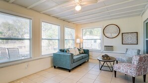A spacious living room with large windows, a blue sofa, a patterned armchair, and a small round table. - Pet-friendly Englewood Home - 4 Mi to Beach! (Englewood)