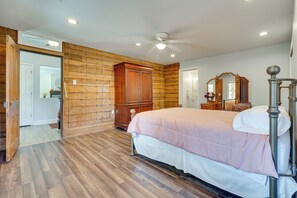 A bedroom with a wooden floor, a bed with a white and pink bedspread, a wooden wardrobe, a ceiling fan, and a mirror. - Spacious & Inviting Jackson Getaway w/ Fireplace! (Jackson)