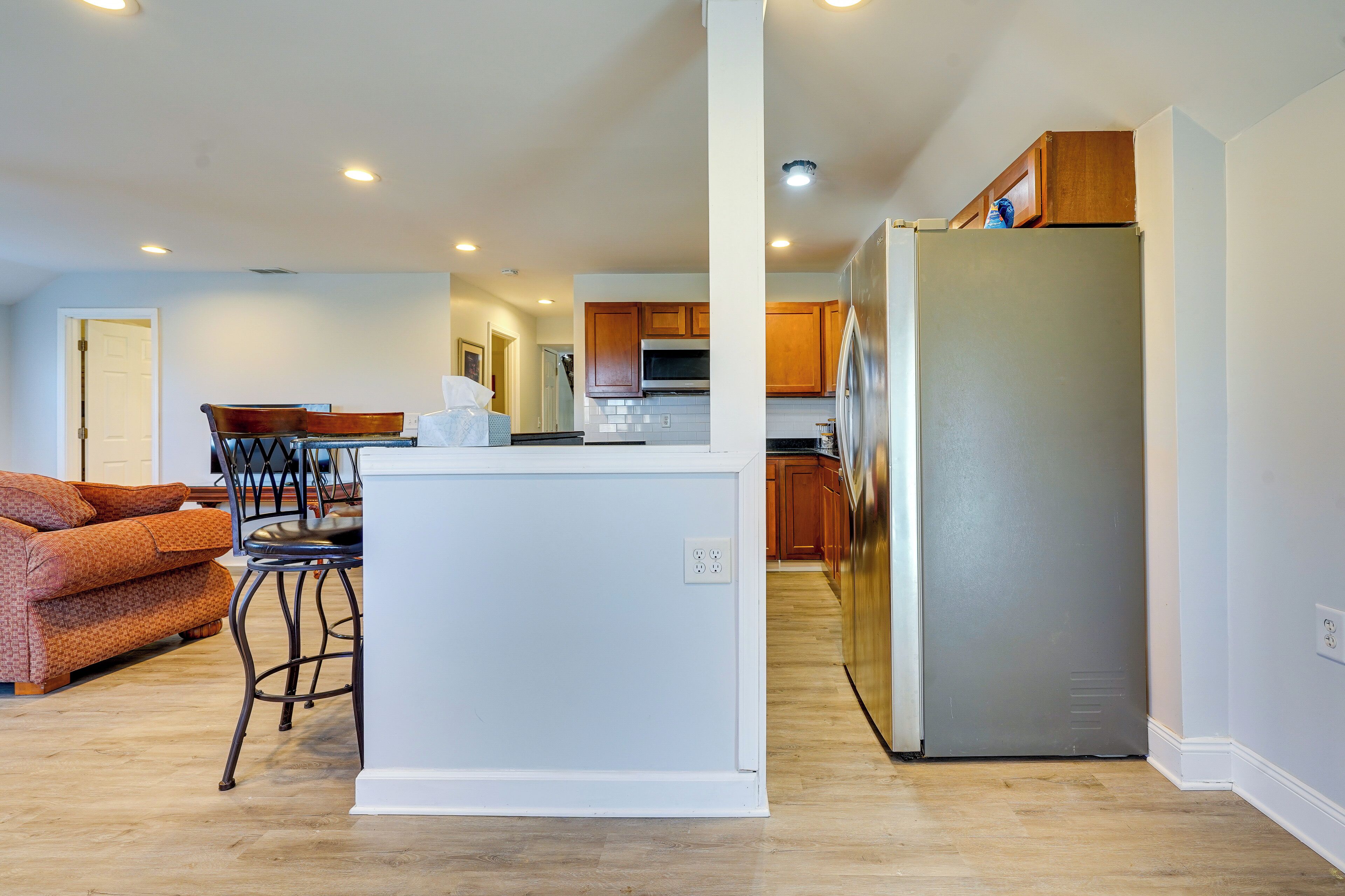 A modern kitchen with wooden cabinets, a stainless steel refrigerator, and a dining area with a patterned sofa and chairs.