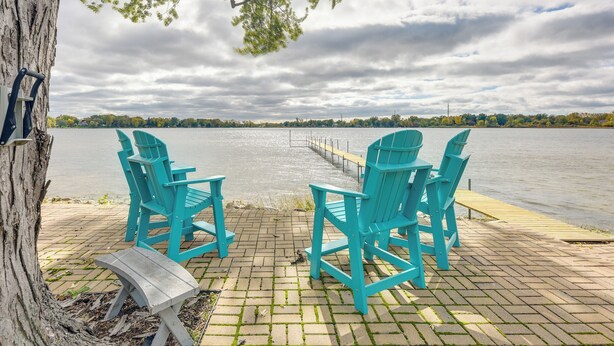 A lakeside seating area with turquoise Adirondack chairs and a wooden bench, overlooking a calm lake with a dock extending into the water. - Lakefront Antioch Cottage w/ Dock & Gas Grill! (Antioch)