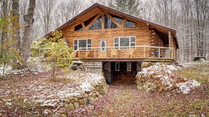Una cabaña de troncos con balcón, rodeada de un bosque nevado.