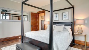 A four-poster bed with a white patterned bedspread, a bedside table with a lamp, and two framed floral artworks on the wall. - Spacious Home in Ramsay: 9 Smart TVs + Pool Table! (Ramsay)