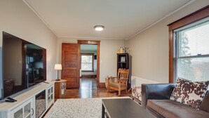 A living room with a TV, sofa, coffee table, and a wooden chair. - Spacious Home in Ramsay: 9 Smart TVs + Pool Table! (Ramsay)