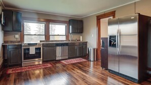 A modern kitchen with stainless steel appliances, dark wooden cabinets, and a red rug on the floor. - Spacious Home in Ramsay: 9 Smart TVs + Pool Table! (Ramsay)