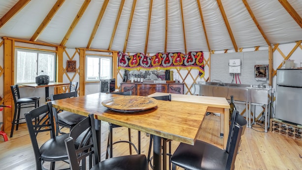 Un vaste espace dédié à la salle à manger, avec une table et des chaises en bois, un coin cuisine équipé d’appareils modernes et une grande fenêtre laissant entrer la lumière naturelle.
