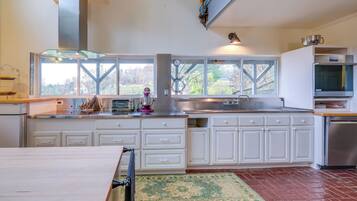 A modern kitchen with white cabinets, a stainless steel range hood, a large window, and a view of the outdoors.