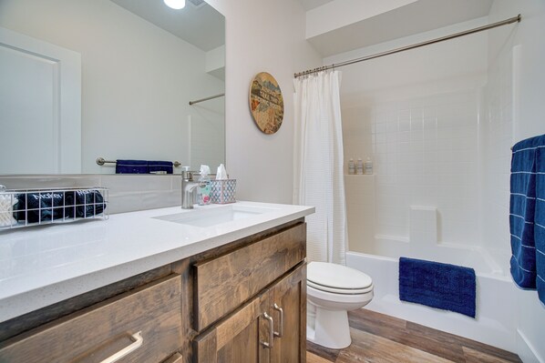 A bathroom with a wooden vanity, a white toilet, a shower with a white curtain, and a towel rack with a blue towel.