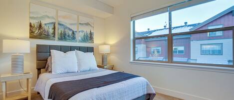 A bedroom with a large bed, two bedside tables with lamps, a headboard, and a window with a view of buildings.