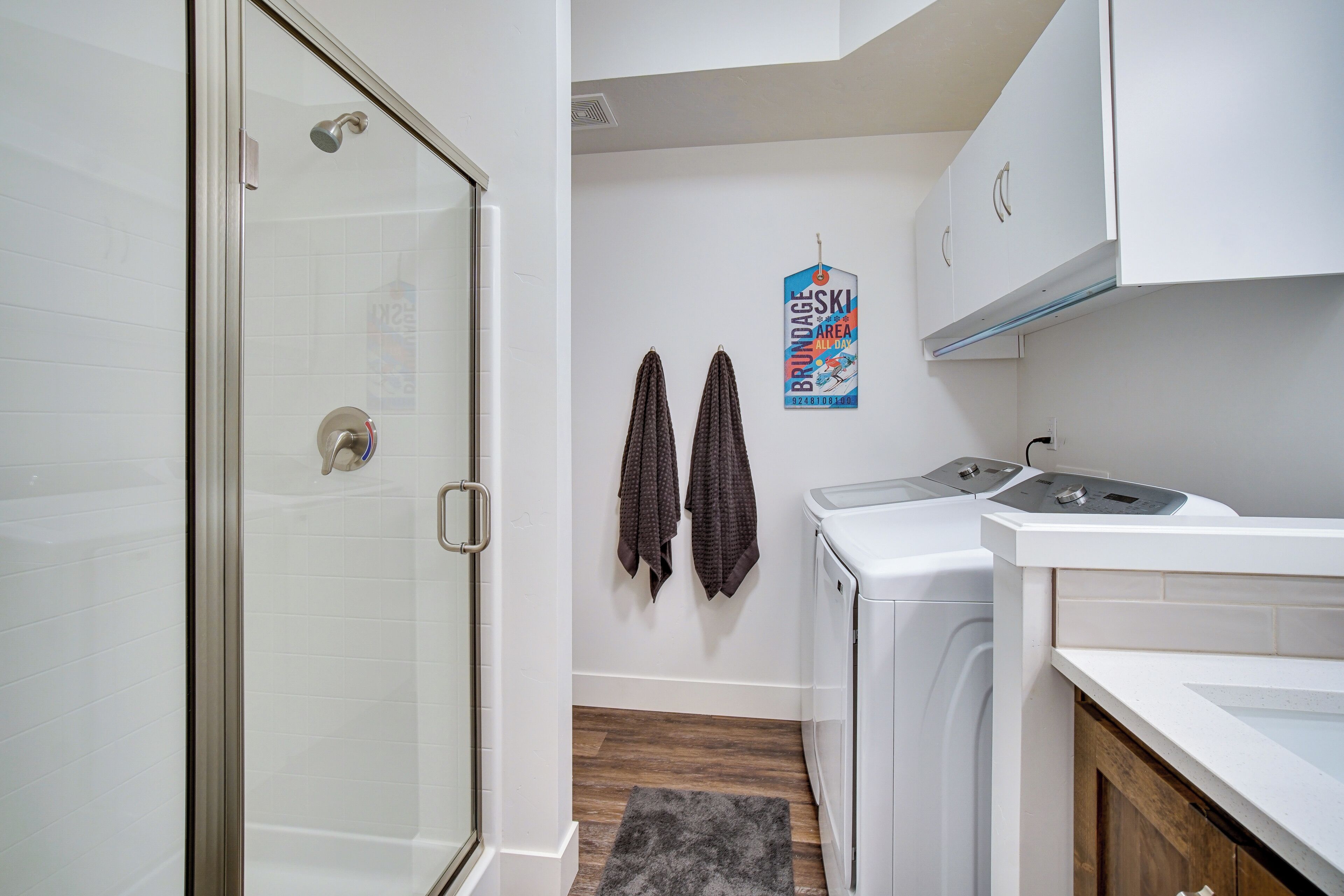 A compact bathroom with a glass shower door, a washing machine, and a dryer. There are two towels hanging on the wall.