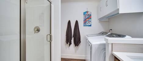 A compact bathroom with a glass shower door, a washing machine, and a dryer. There are two towels hanging on the wall.