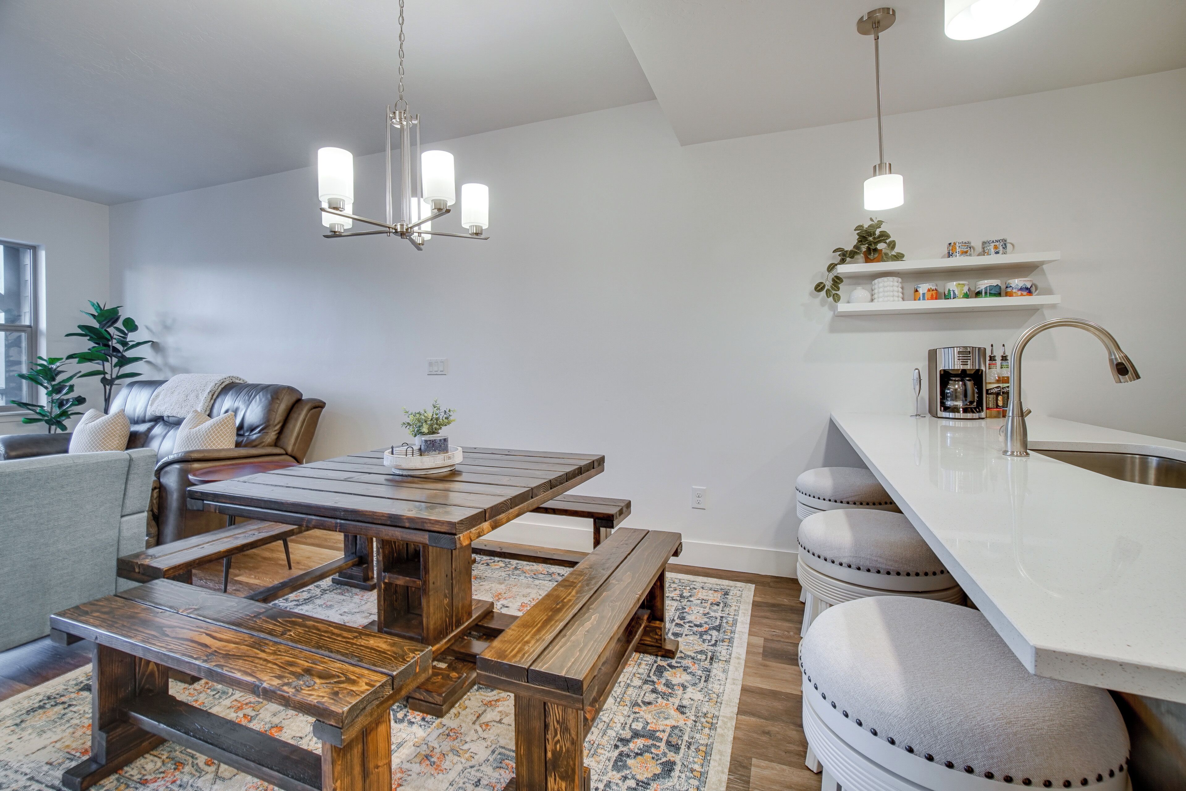 A modern kitchen with a wooden dining table, bench seating, a built-in island with a sink, and pendant lighting.