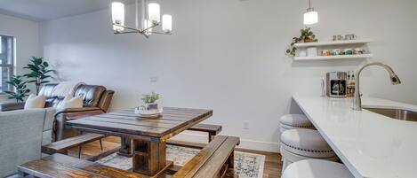 A modern kitchen with a wooden dining table, bench seating, a built-in island with a sink, and pendant lighting.