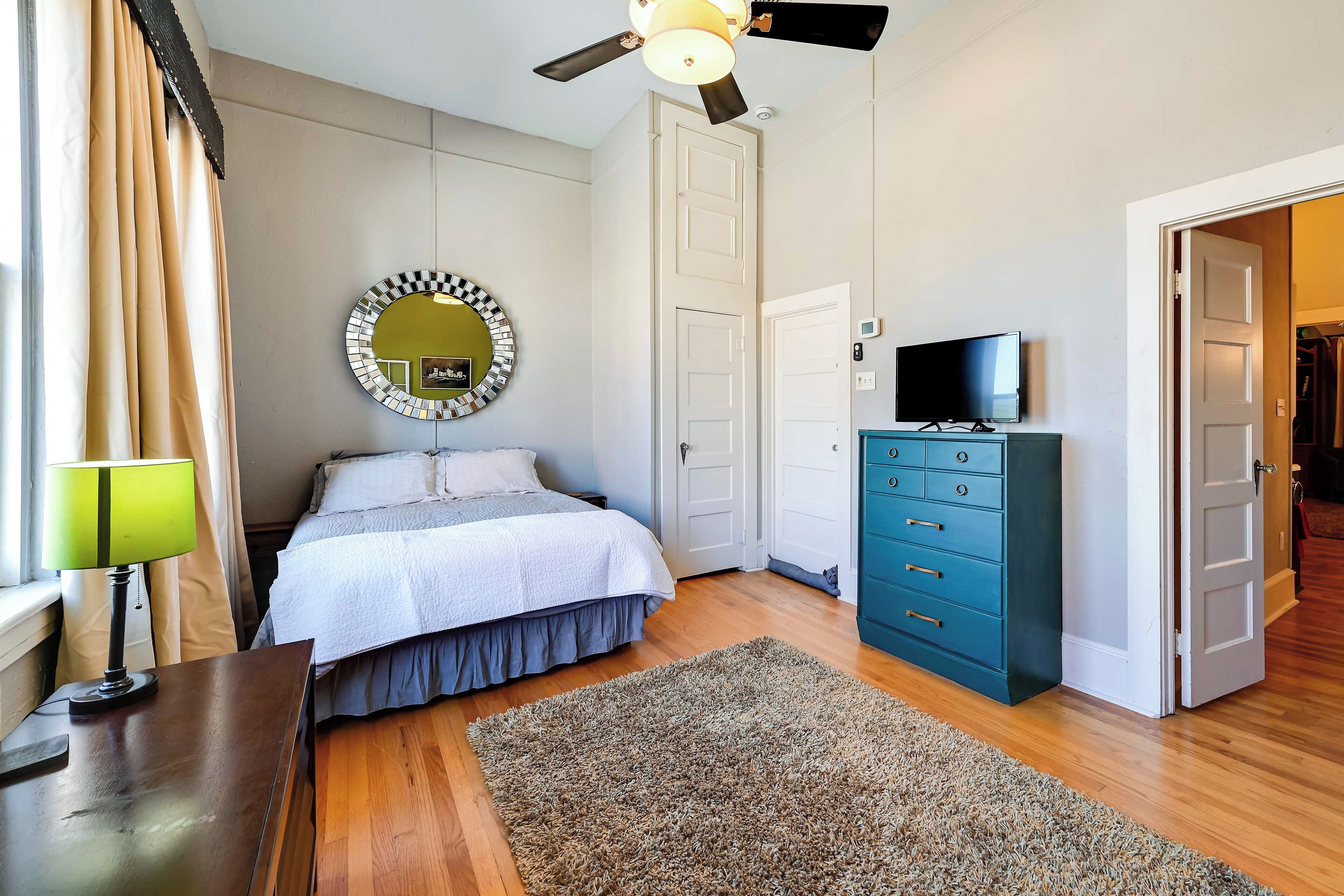 Un dormitorio con cama, cómoda, televisor, ventilador de techo y espejo.
