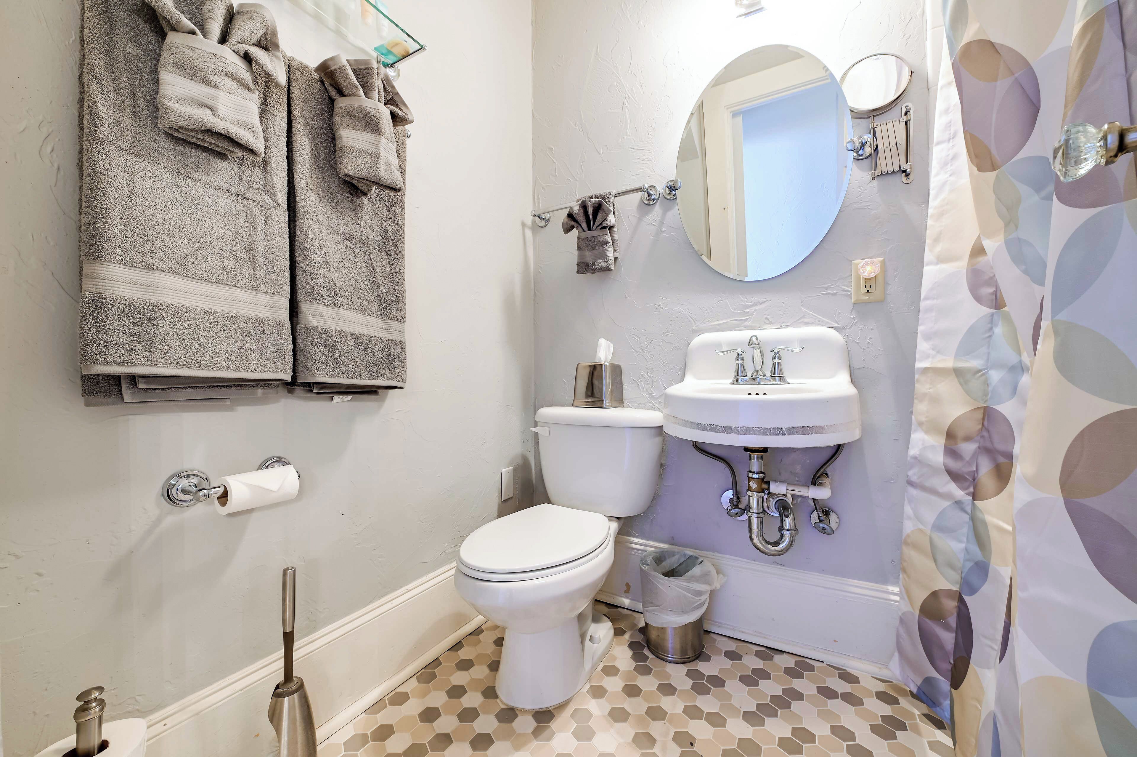 A bathroom with a toilet, sink, and mirror. There are towels hanging on a rack and a trash can.