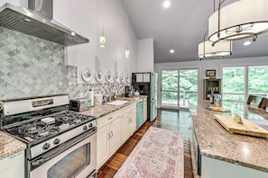 A kitchen with a gas stove, oven, and microwave, a large window, and a view of greenery outside. - Riverwood: South Haven Retreat on 10 Acres (South Haven)