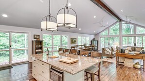 A spacious kitchen with a large island, wooden flooring, and large windows offering a view of the outdoors.