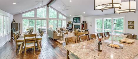 Una cocina amplia con una isla grande, una mesa de comedor de madera y sillas, rodeada de ventanas grandes y un techo alto.