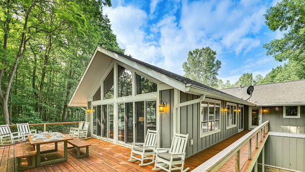 A wooden deck with outdoor furniture, a covered patio, and a view of a forested area.