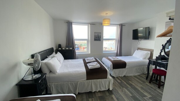 A hotel room with two beds, a desk, a TV, and a view of the city. - The Lady Hamilton B&B (Portsmouth)