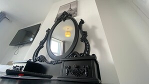 A black vanity with an ornate mirror, a flat-screen TV mounted on the wall, and a framed picture above the mirror. - The Lady Hamilton B&B (Portsmouth)