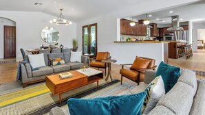 A modern living room with a sofa, coffee table, and chairs, a kitchen with wooden cabinets and stainless steel appliances, and a dining area with a table and chairs. - Mirador Desert Oasis – Mediterranean Escape (Palm Springs)