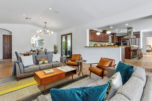 Un salon moderne comprenant un canapé, une table basse et des fauteuils, une cuisine avec des meubles en bois et des appareils électroménagers en acier inoxydable, et un coin repas avec une table et des chaises.