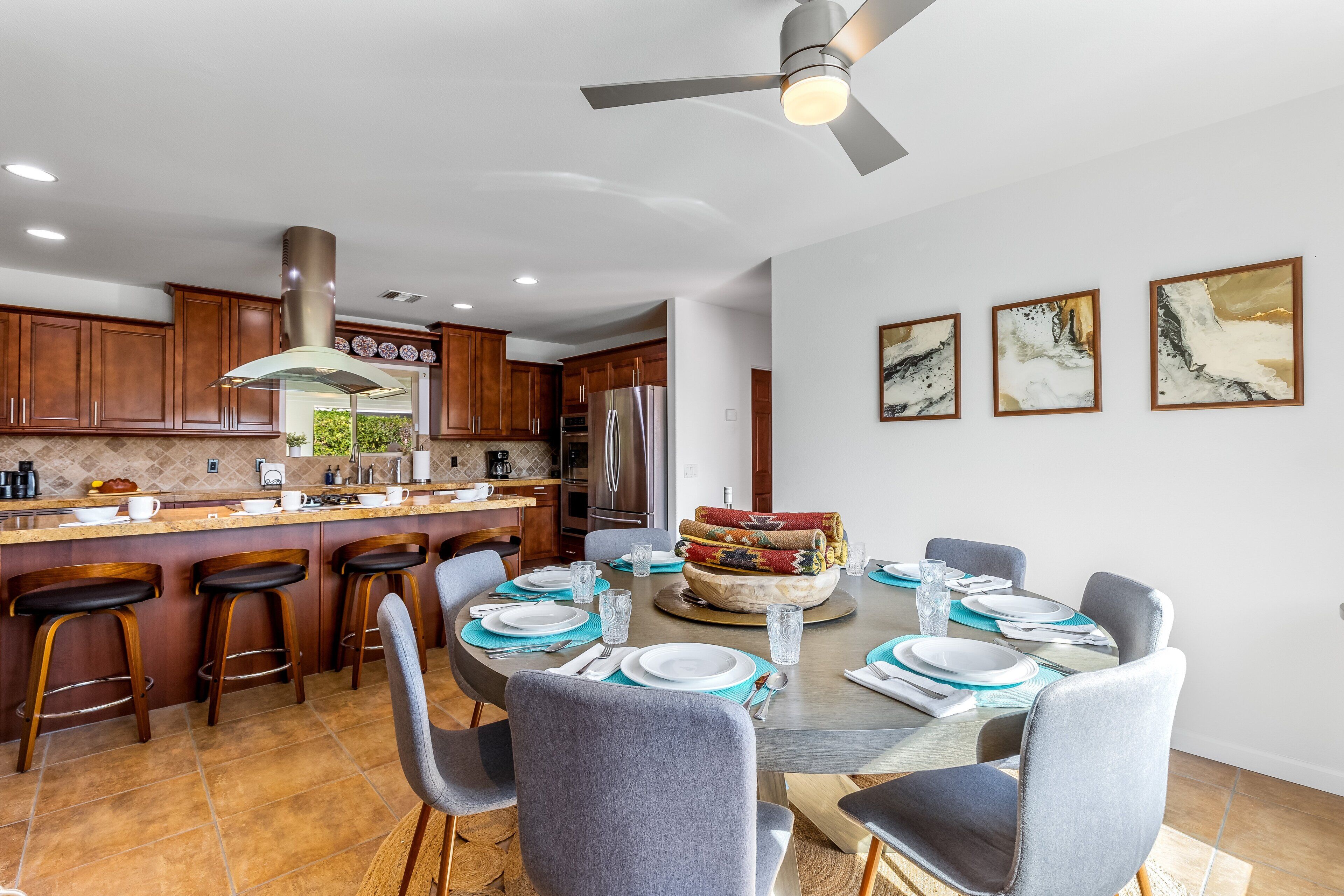 A modern kitchen with wooden cabinets, a stainless steel refrigerator, and a dining area with a round table set for six.